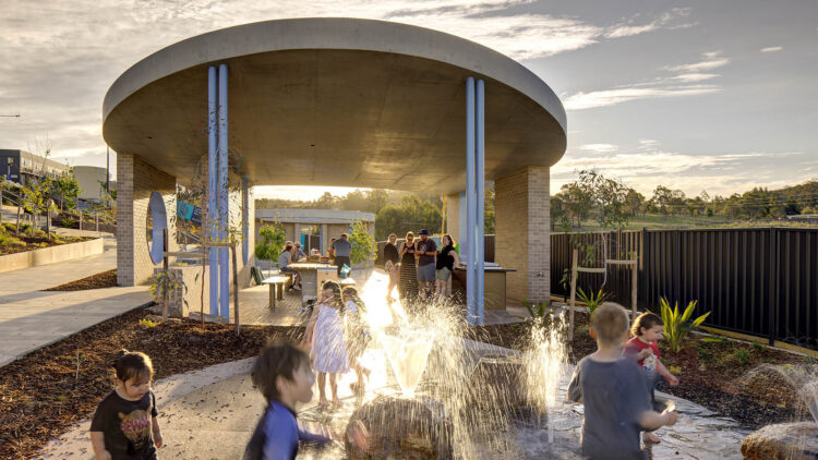 Public architecture amenities concrete canopy with children and families playing in the water fountains